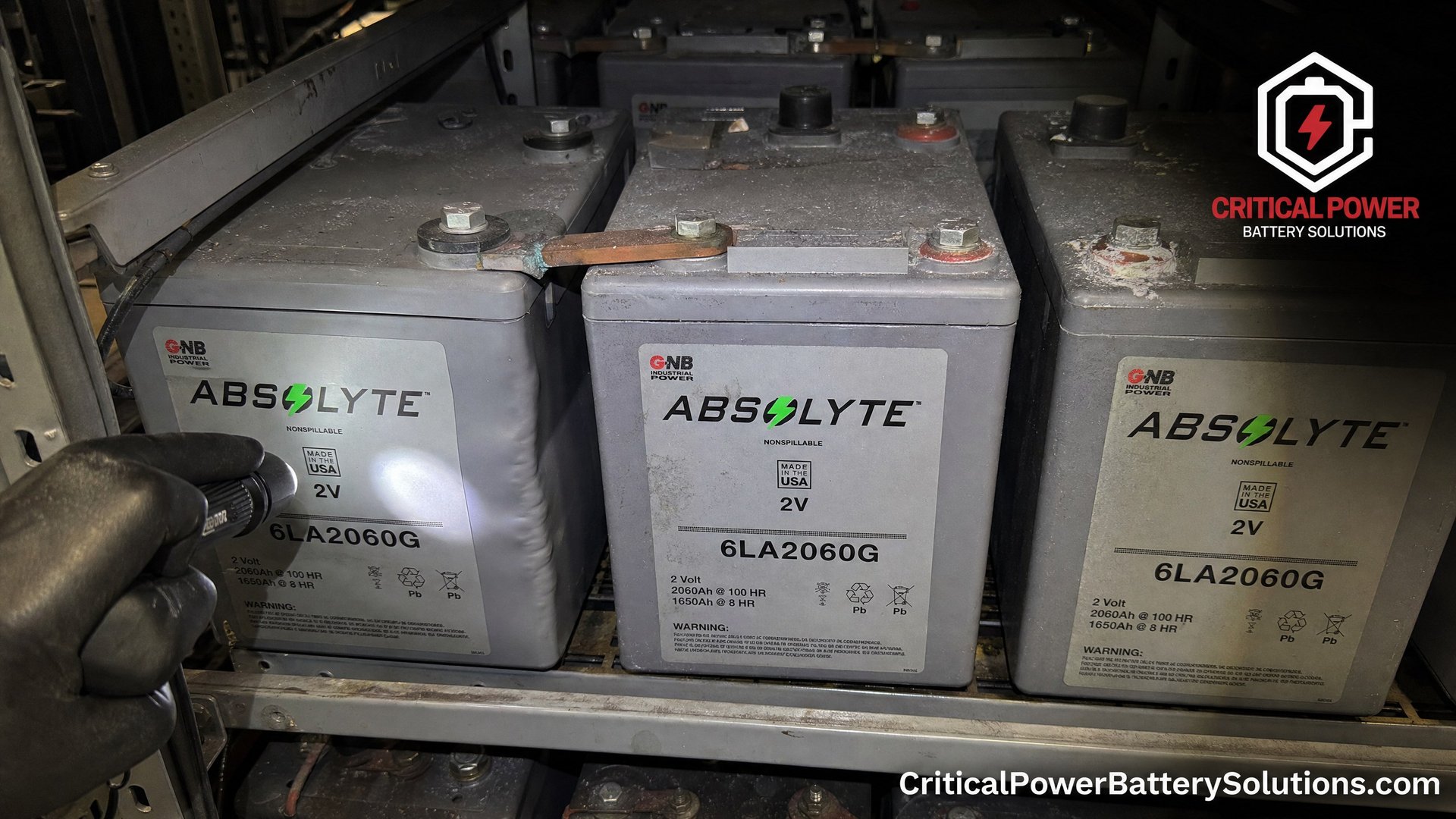 Close-up of aging GNB Absolyte 2V battery cells showing visual failure symptoms including a swollen case and terminal sulfation.