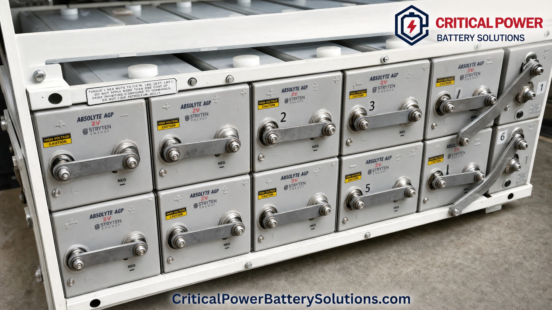 Close-up of Stryten Energy Absolyte AGP 2V VRLA AGM battery cells showing round stainless steel terminal posts, flat aluminum bus bars, and numbered cell identification in industrial steel rack.